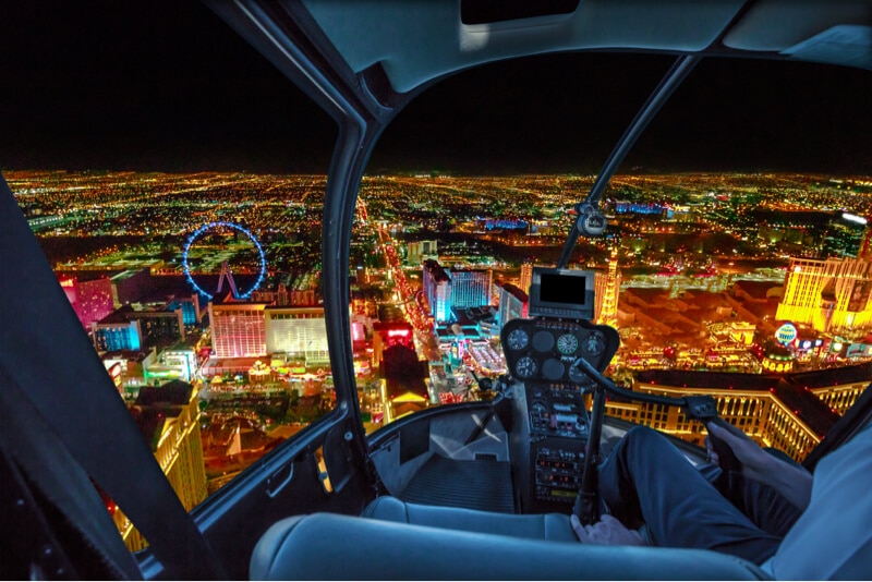 Helicopter cockpit view flying over Las Vegas Strip at night with city lights and landmarks illuminated