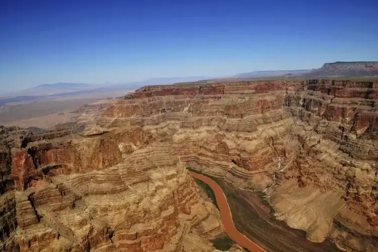 Aerial view of the Grand Canyon with layered rock formations and the Colorado River winding through the valley.